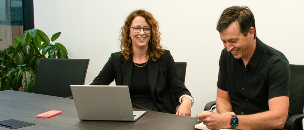 A woman and a man smiling at a board room table accompanied by text that reads, “Chief Technology Officer Maureen Kinnear talks all things leadership”.  