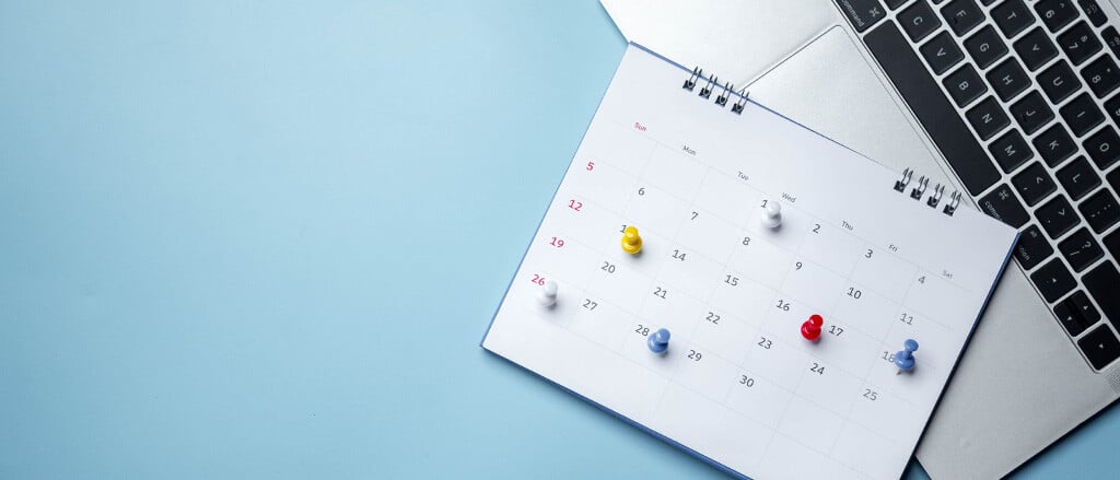 A laptop keyboard and a calendar with pins on dates accompanied by text that reads, “Ensure your staff is paid on time with the payroll processing & delivery dates for December 2024 & January 2025”.  