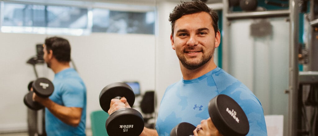 An individual holding up free weights accompanied by text that reads, “See gains in employee wellness with physical, mental, emotional & social health supports”.  