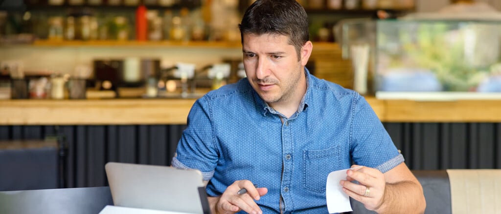 A man holding a receipt and looking at a laptop accompanied by text that reads, “Payroll. Xero users: save time with our journal entry integrations”.  