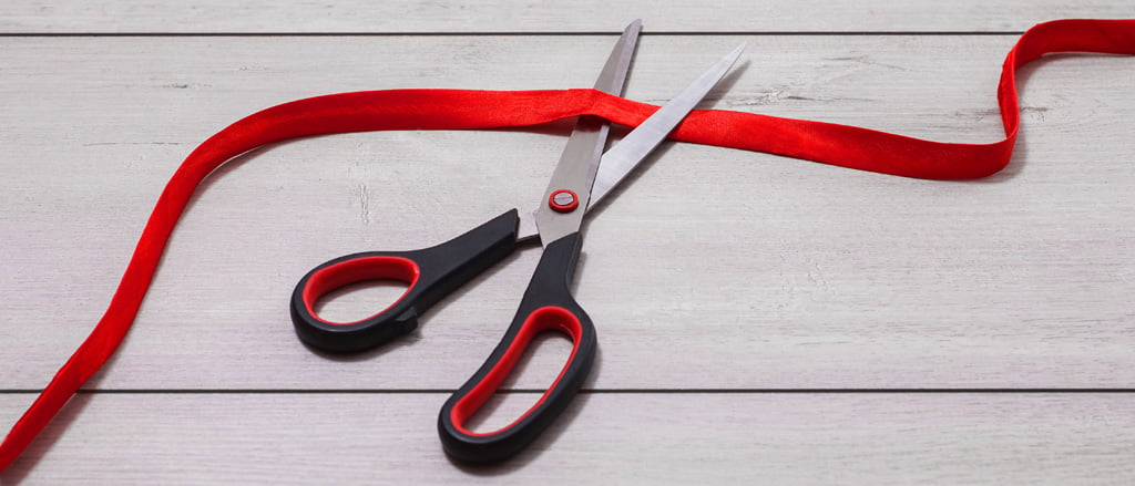 A pair of scissors cutting through a red ribbon accompanied by text that reads, “10 payroll & HR administrative hurdles we help small businesses tackle”.  