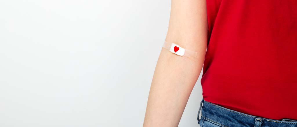 An arm with a Band-Aid on it with a small heart. Text reads, “pay it forward”.  