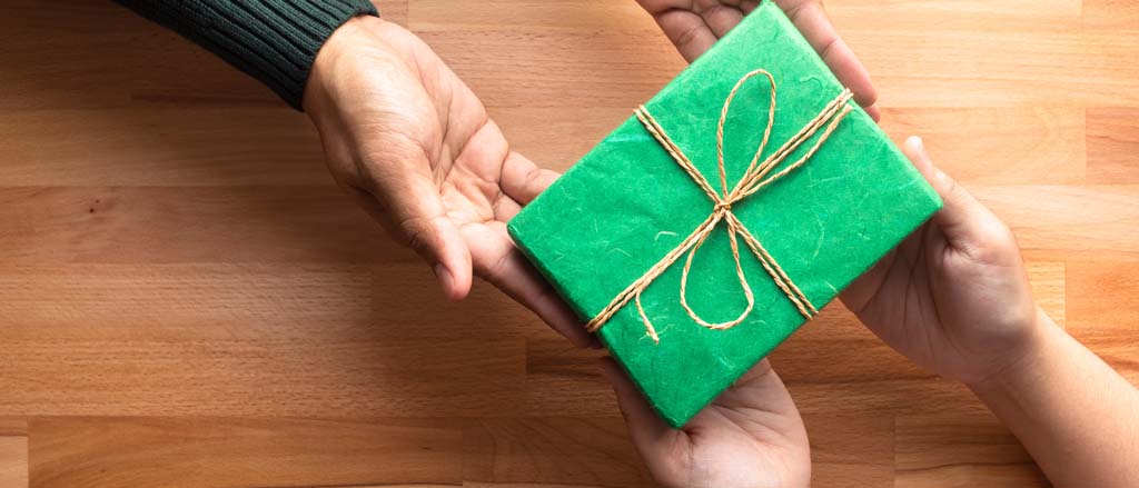 Two hands holding a gift-wrapped present. Text reads, “Pay it Forward”.  