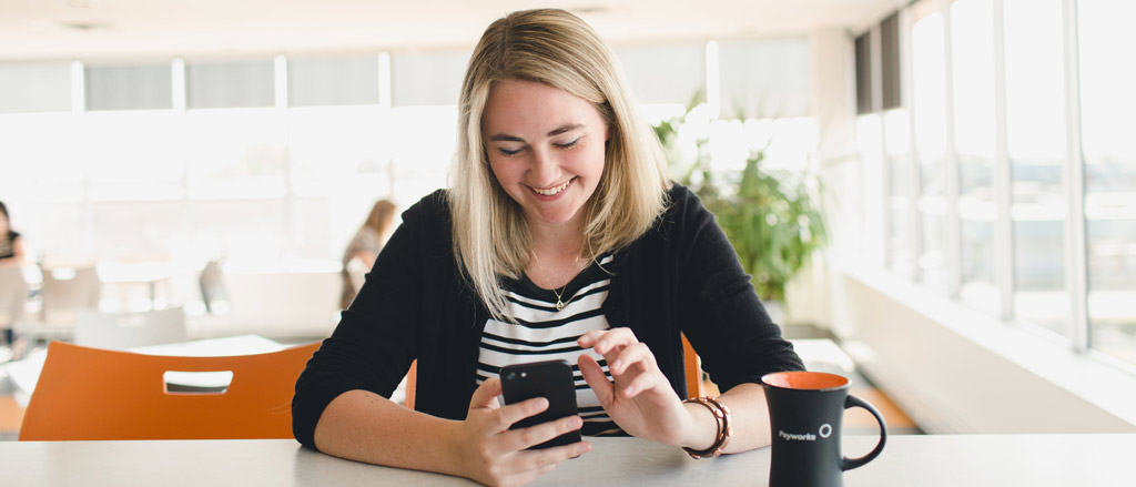 Une femme dans sa mi-vingtaine assise à un comptoir regarde son téléphone en souriant.