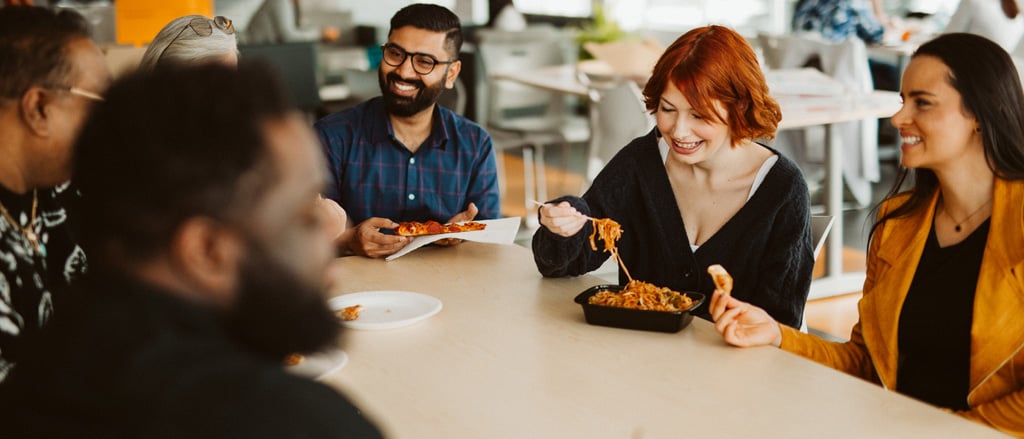 Six employees sitting around a lunchroom table eating accompanied by text that reads, “New video… why Payworks is such an engaging place to work”.  