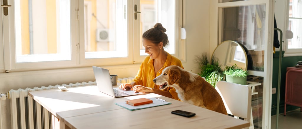A person working on a laptop at their kitchen table with their dog accompanied by text that reads, “what you need to know; updates to Form T2200”.  
