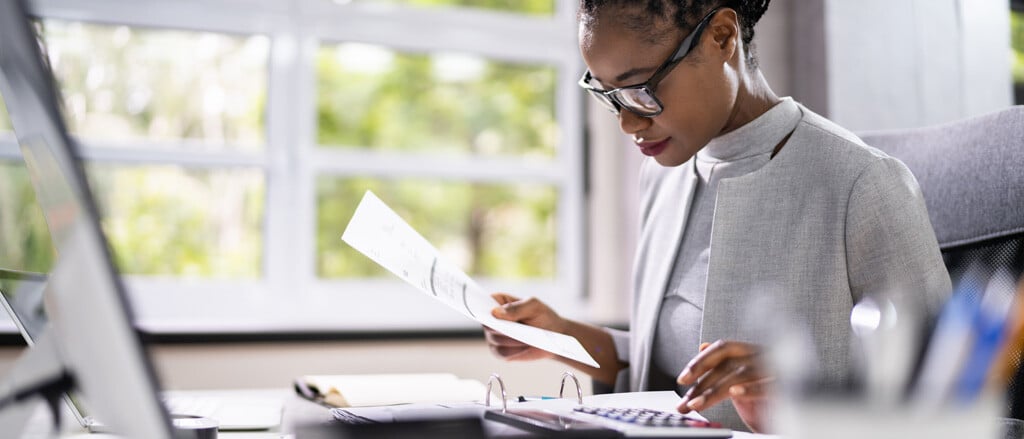 A woman looking at a piece of paper while typing on a calculator accompanied by text that reads, “What’s new for year-end 2024”.  