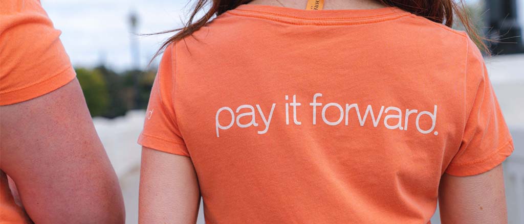 Four Payworks staff standing on a beach holding two garbage bags. Text reads, “pay it forward”.   