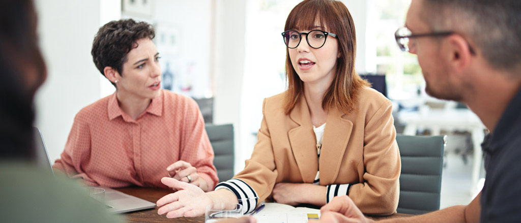 Four people in an office, two men and two women, having a serious conversation. 