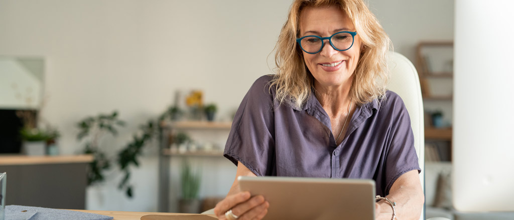 Text reads, “9 easy steps to get you through the payroll year-end process”.  Photo of a smiling woman seated at a desk while using an iPad tablet.