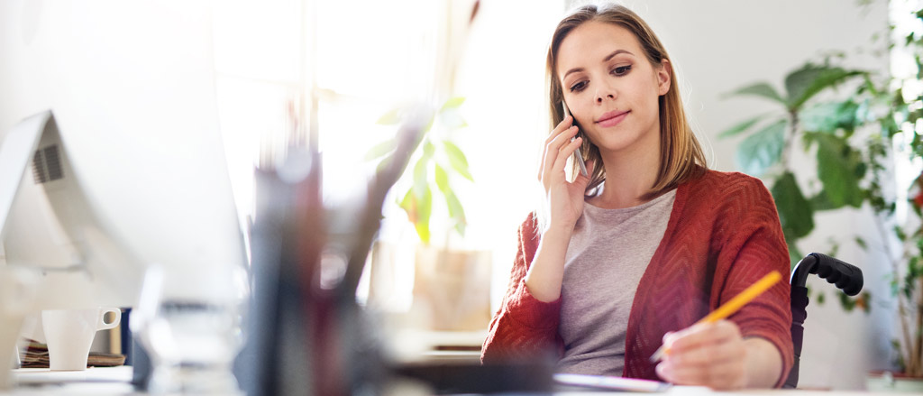 A woman talking on the phone and writing notes. Text reads, “Absence Management; Harmonize time off requests, approvals, communication and reporting”.  