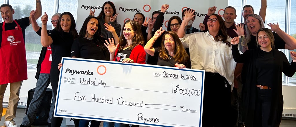 A group of Payworks volunteers around a giant cheque for $500,000. Text reads, "Pay it Forward". 