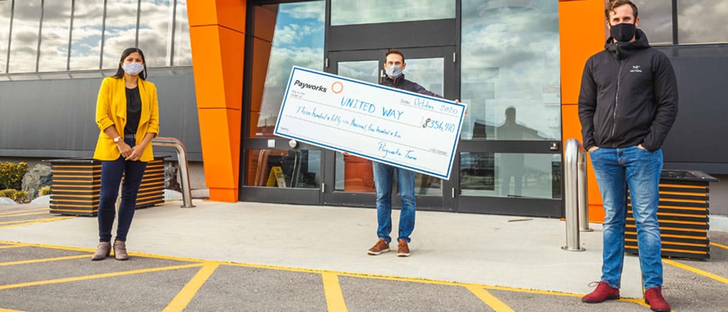 Three members of the Payworks United Way Workplace Committee jumping outside with a giant cheque for $356,410.32. 