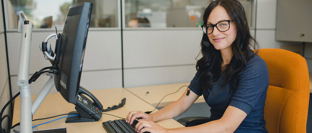 A customer service representative sitting at their desk with a headset on. Text reads, “According to our in-house experts… how to hire someone with a service mind-set”. 